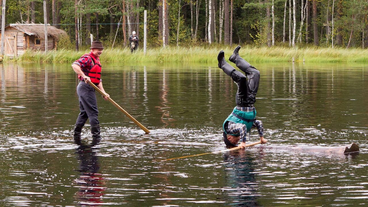 One person standing and other person standing on his head on a log in the water