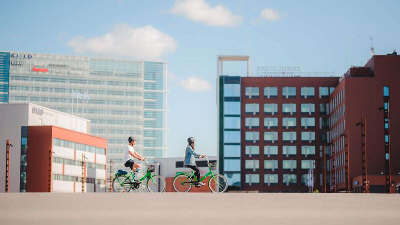 Two persons cycling in front of the Solo Sokos Hotel Paviljonki.