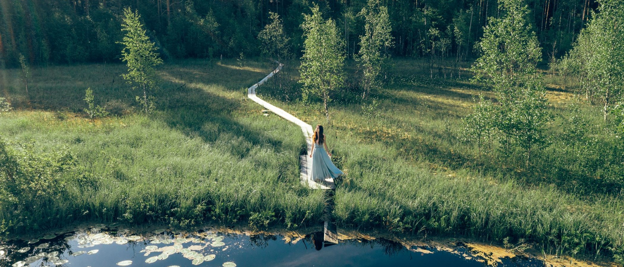 Henkilö selin pitkospuiden päässä järven rannalla.