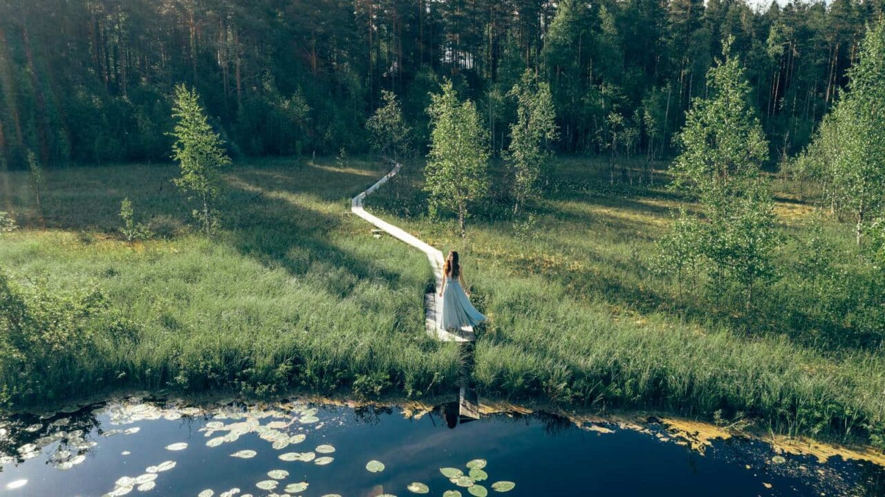 Henkilö seisoo lammen rannalla pitkospuilla.