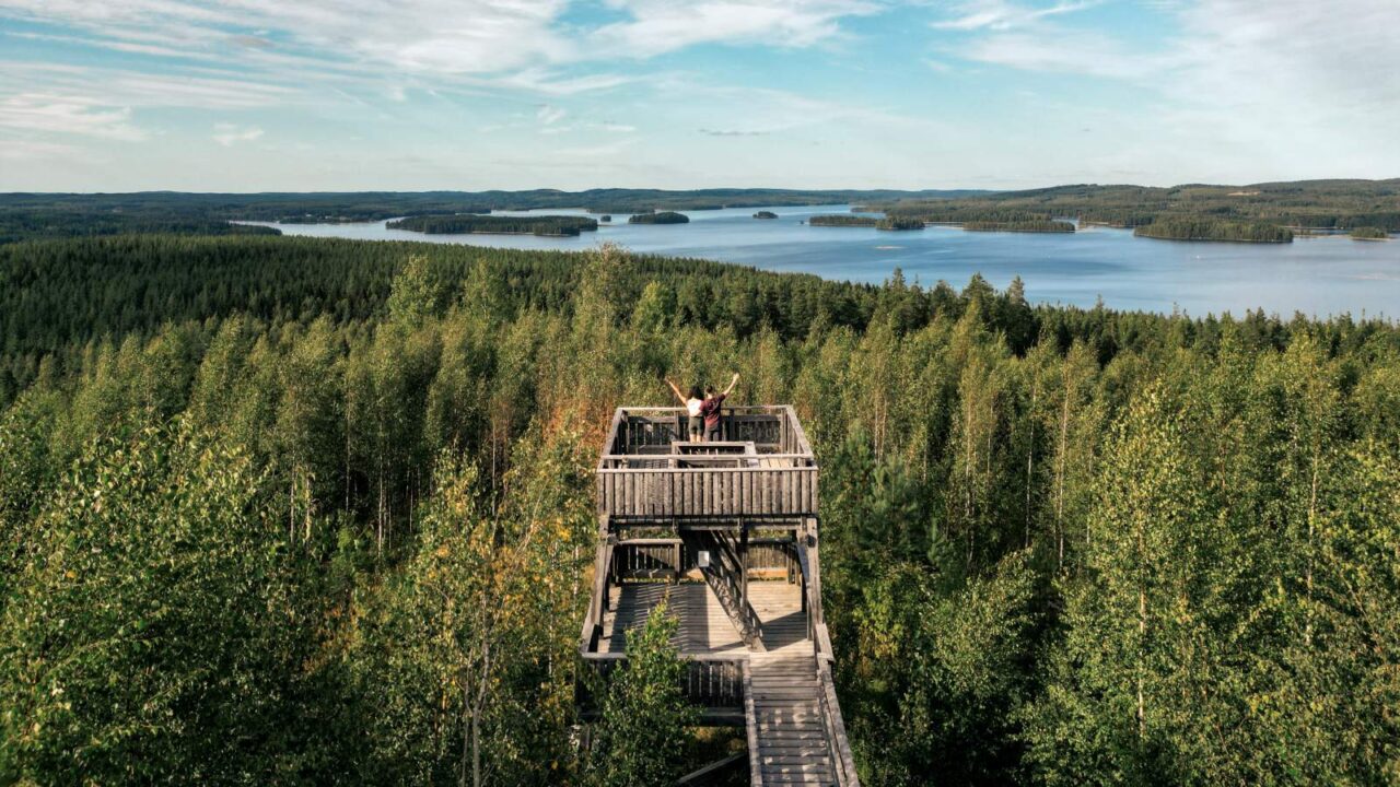 Kaksi henkilöä Äänemäen näkötornissa, jota ympäröi metsä- ja järvimaisema.