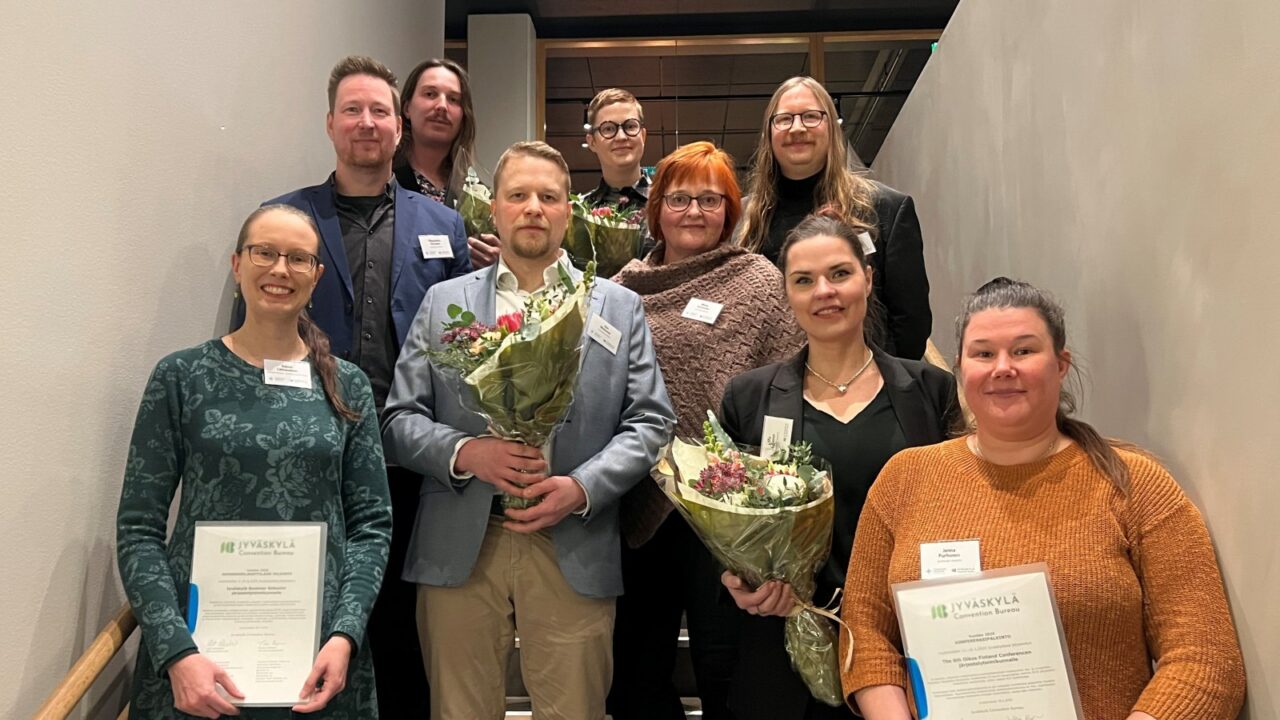 Eight people standing at a staircase and holding flower bucket and diplomas in their hands.