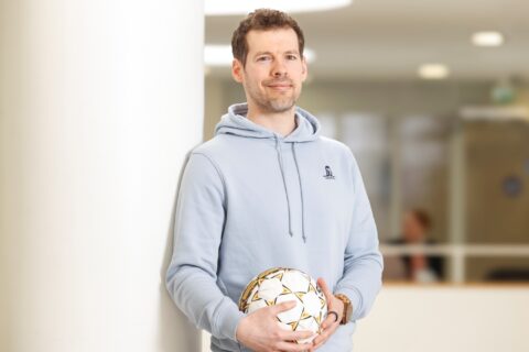 Henkilö seisoo jalkapallo kädessään valkoisen pylvään vieressä.