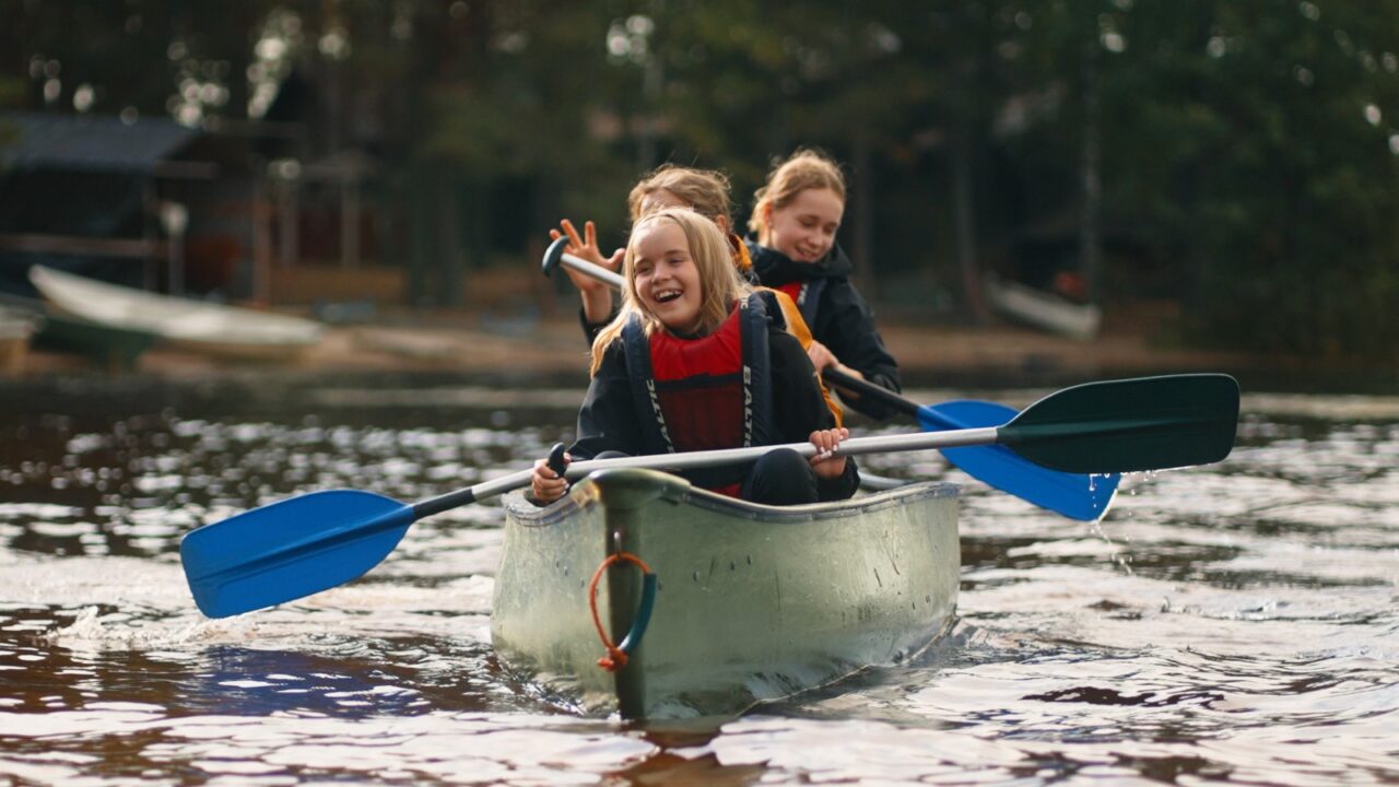 Three children are paddling in a canoe.