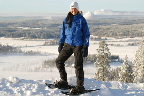 A person stands on top of a hill wearing snowshoes.