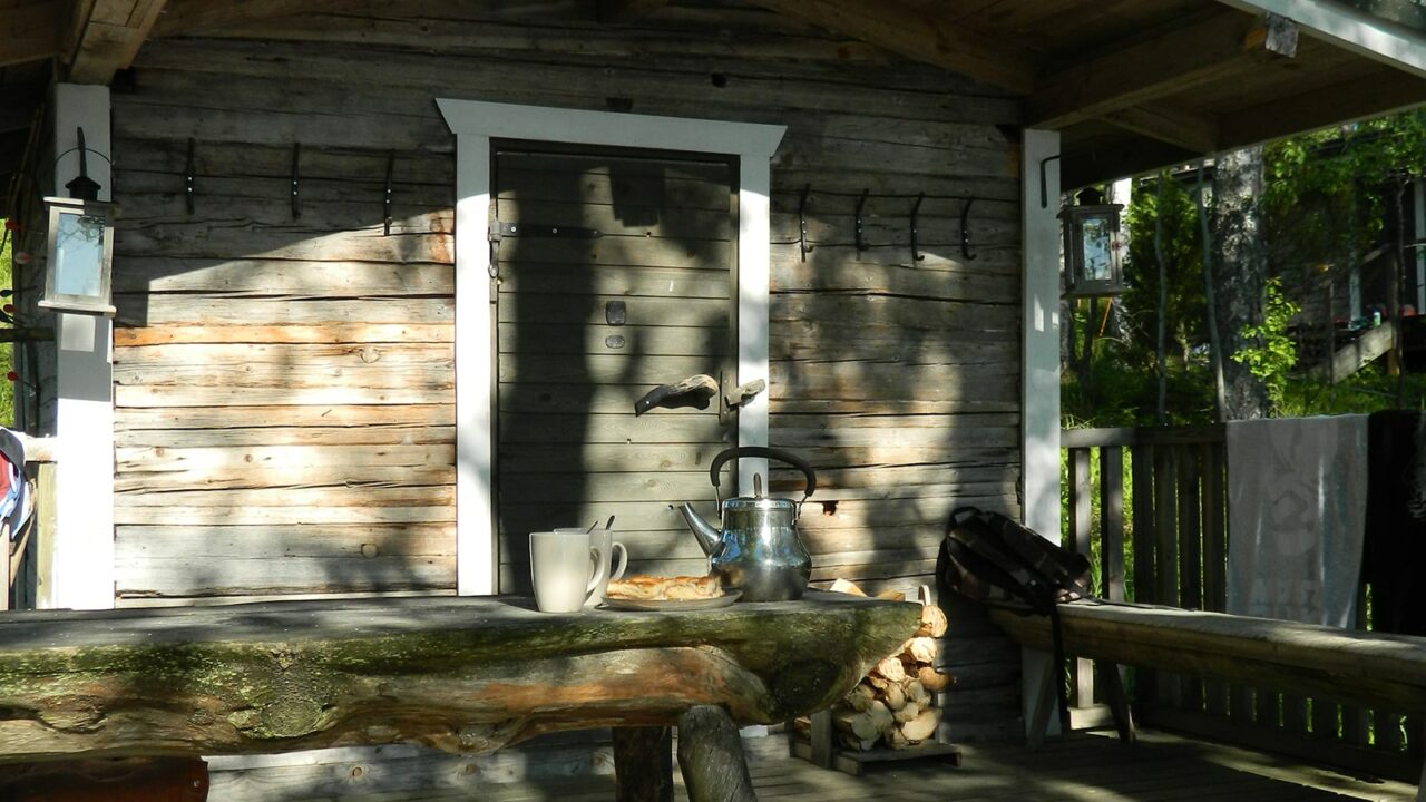Kahvipannu ja kahvimukeja penkillä saunarakennuksen edessä.