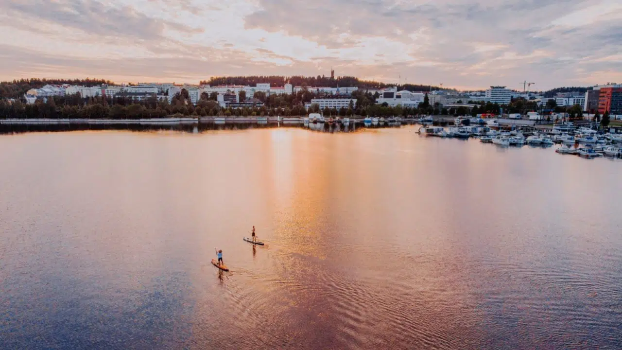 Zwei Personen auf SUP-Boards auf dem See vor dem Hafen von Lutakko in Jyväskylä, dem finnischen Seengebiet