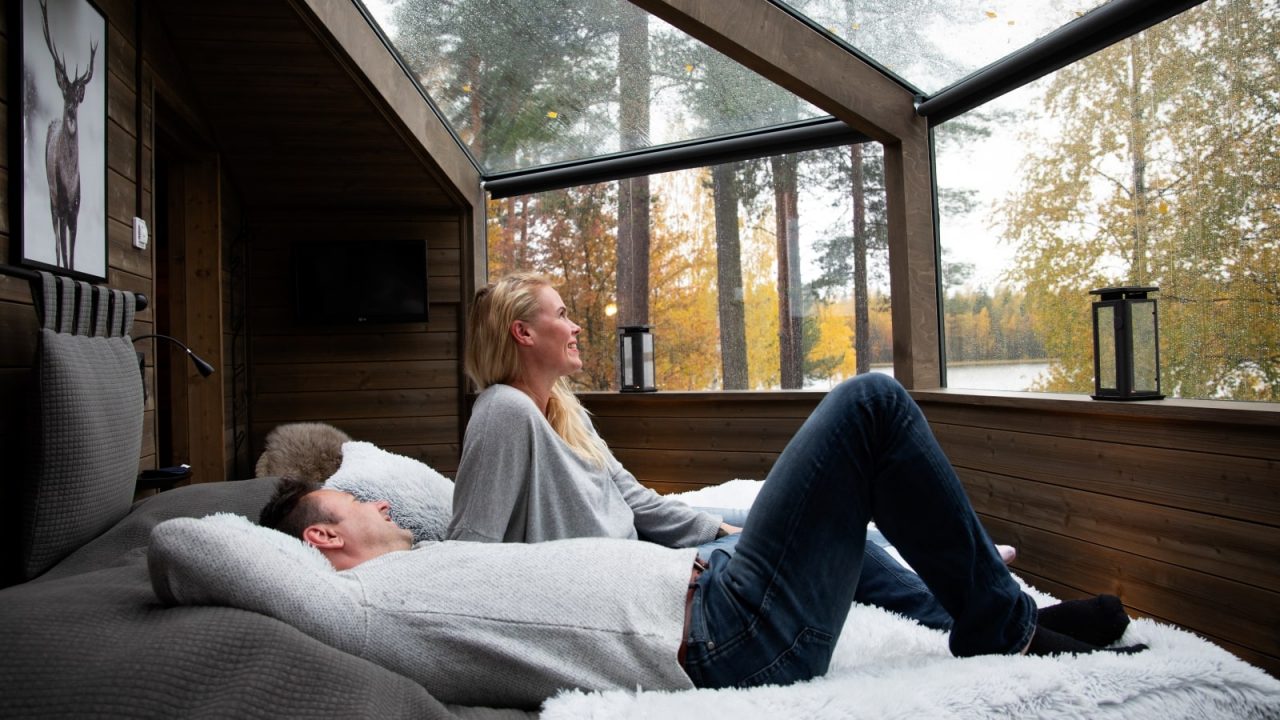 Kaksi ihmistä makoilee sängyllä Revontuli Resortin lasi-iglussa.