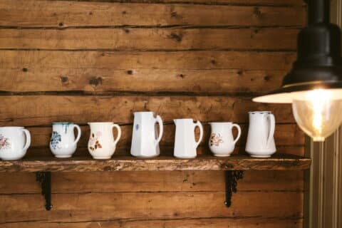 Old porcelain jugs lined up on a wall shelf.