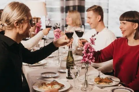 Henkilöitä ruokapöydässä kippistämässä punaviinillä