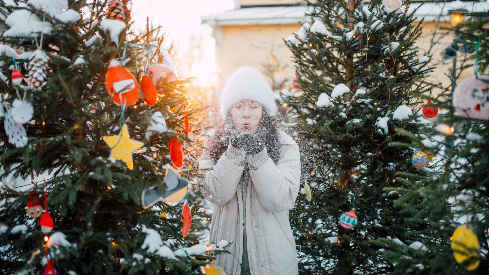 A person stands among the decorated Christmas trees in Toivola old courtyard and blows the snow in their hands into the air.