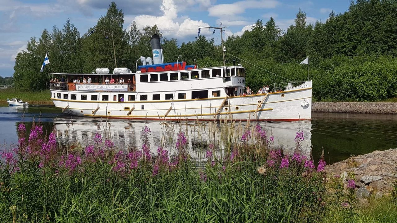 Laiva järvessä, jonka ympärillä kukkia sekä metsää.