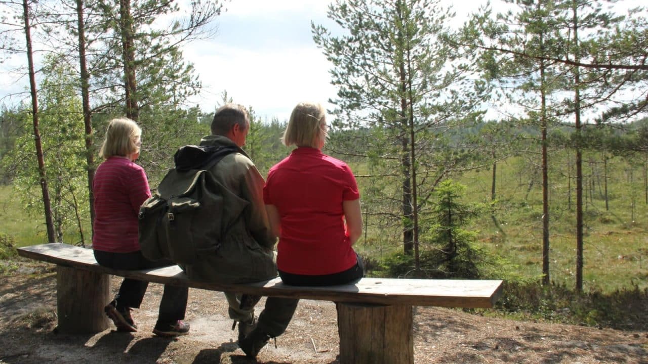Kolme henkilöä istumassa penkillä metsässä.