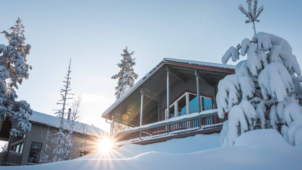 Puinen huvila lumisessa maisemassa. Talon edessä on luminen kuusi ja talon takaa paistaa aurinko.