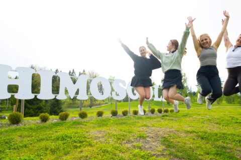 Henkilöt hyppäävät Himoksen logon edessä nurmikolla.