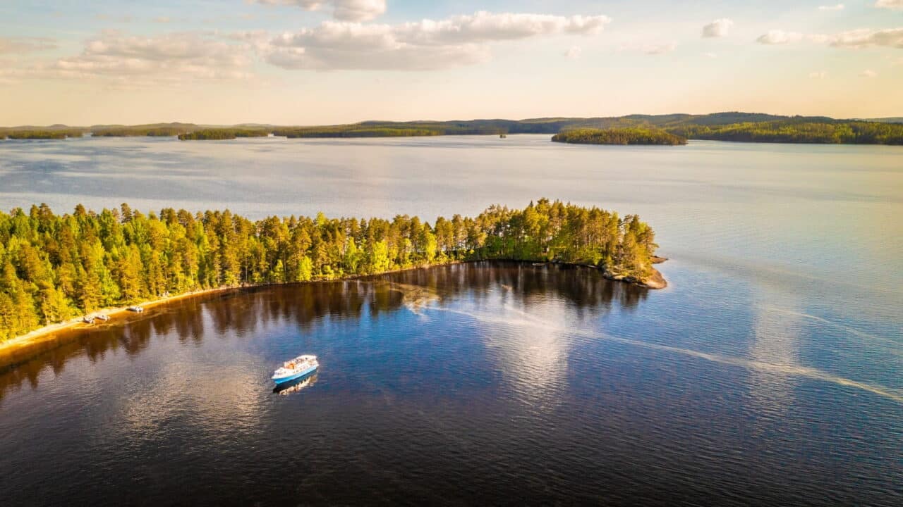 Kaunis järvimaisema, jossa puinen niemi ja laiva edustalla.