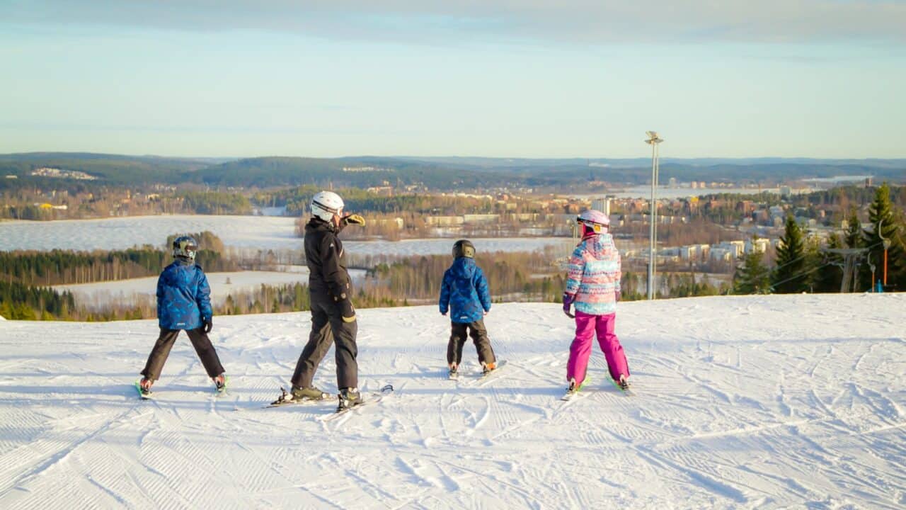 Aikuinen ja kolme lasta Laajavuoren rinteessä suksilla.