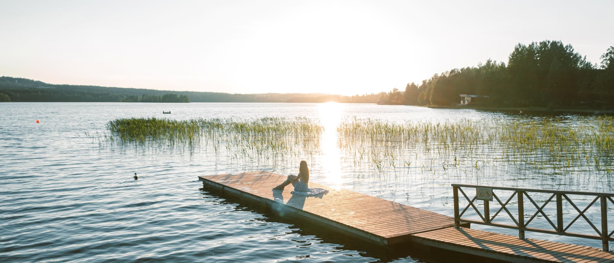 Henkilö istuu laiturilla ilta-auringossa.