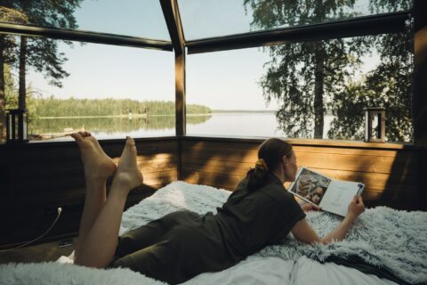 Henkilö lukemassa kirjaa sängyllä lasi-iglussa kesällä.