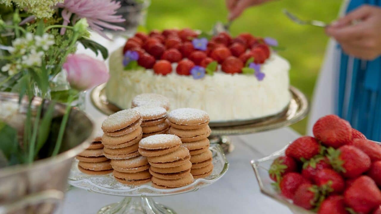 Auf dem Serviertisch stehen Kekse, Erdbeeren und Sahnetorte.