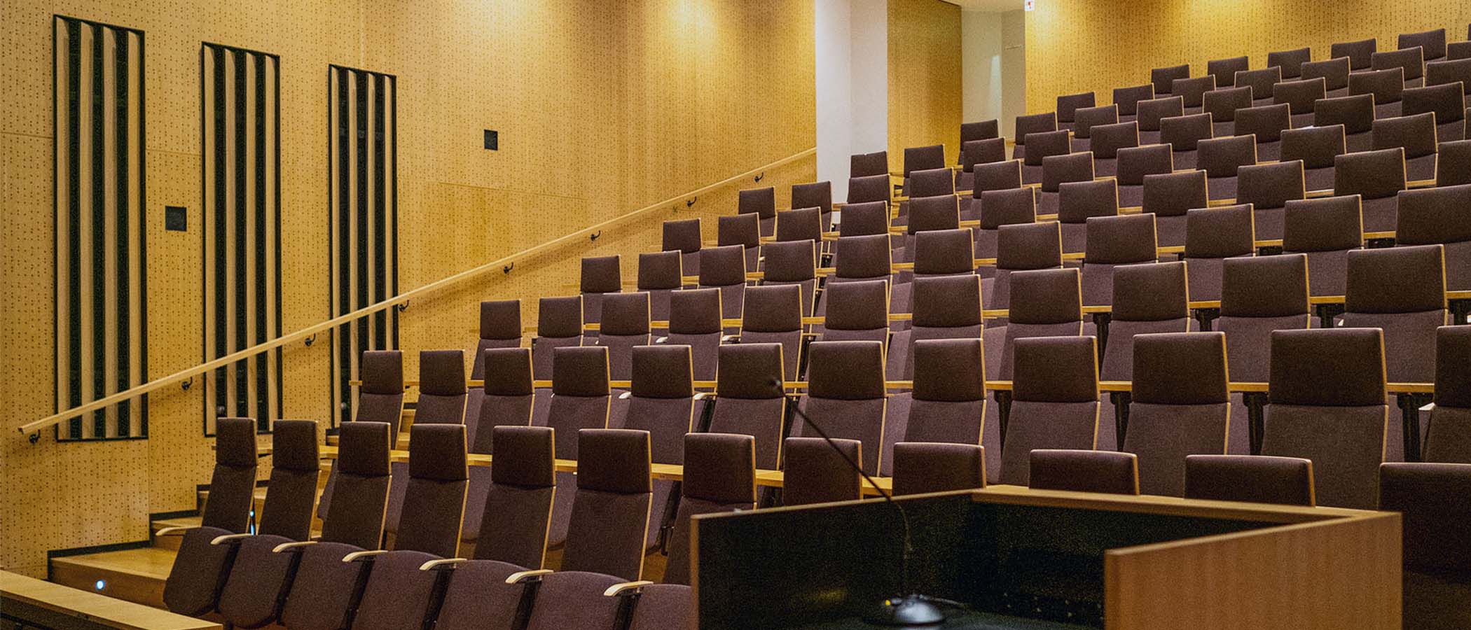 Viininpunaisia pehmustettuja auditorioistuimia nousevassa katsomossa. Puuseinäkkeet