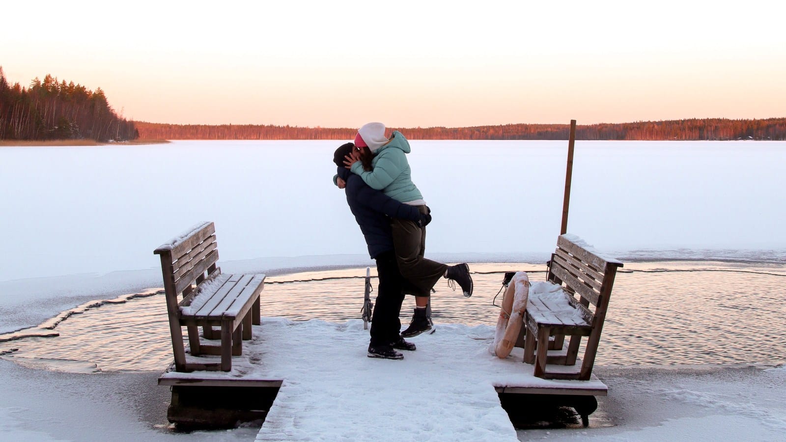 Two people hugging on a small snowy pier.