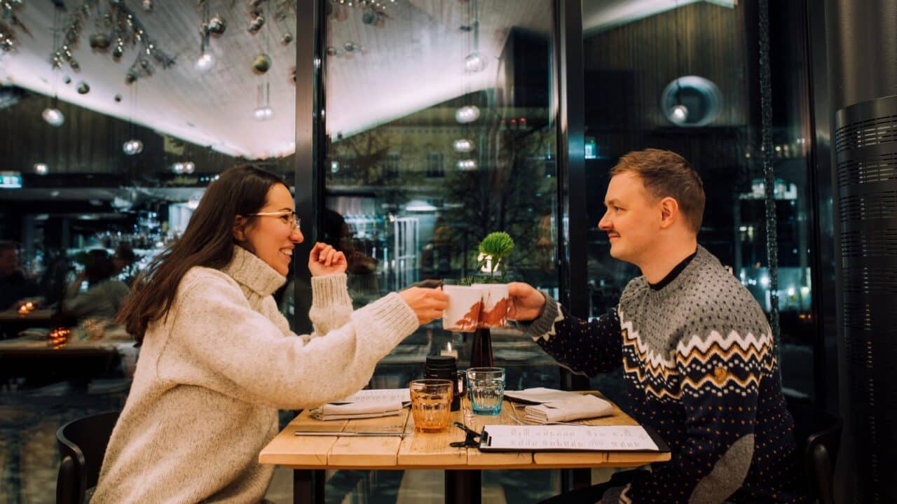 Two people are sitting at a restaurant table, sipping on mugs.