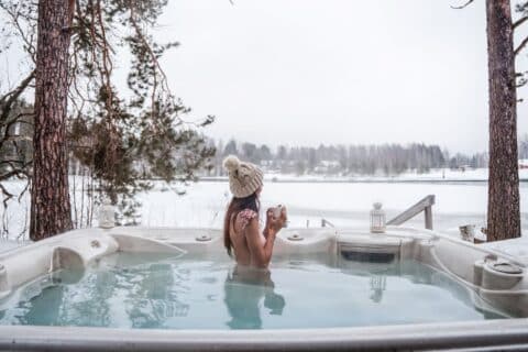 A person relaxes in an outdoor hot tub in a wintery landscape.