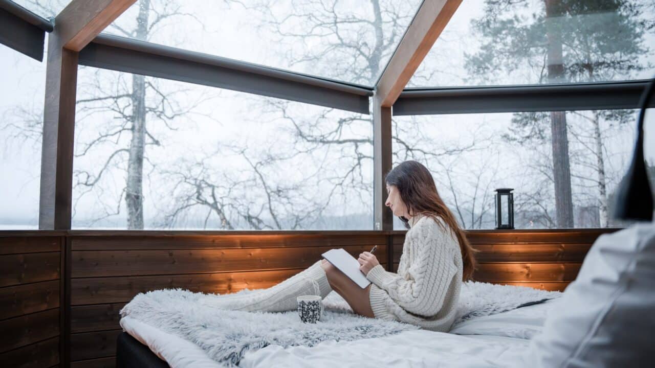 A person sits and writes in a notebook in an igloo hotel room.