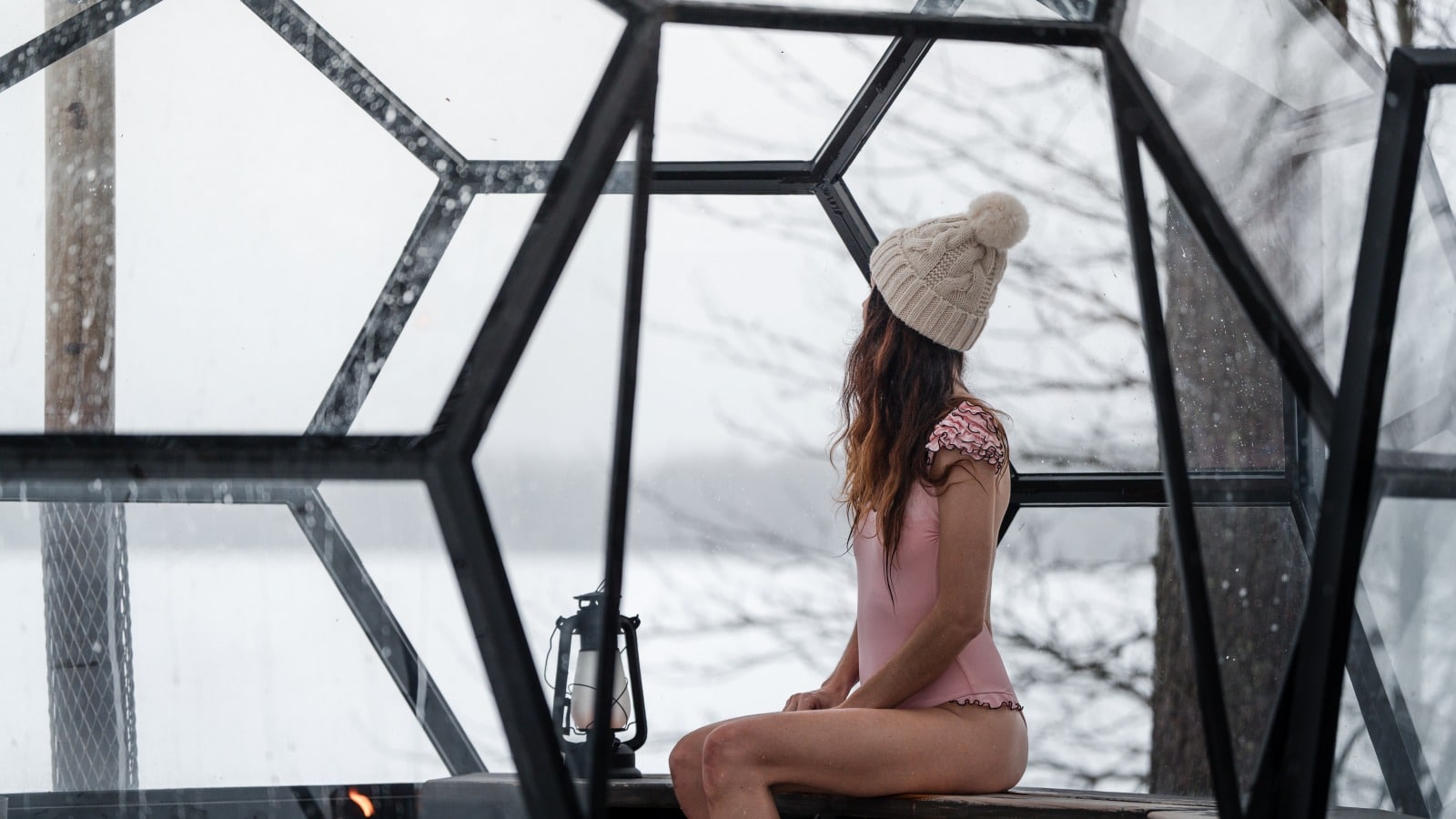 A person sits in a glass igloo and looks out.