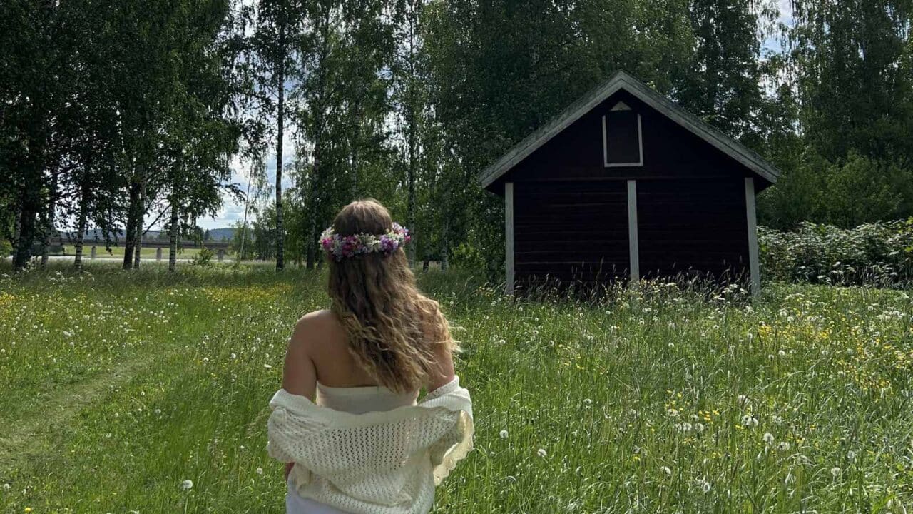 Eine Person steht auf einem Sommerfeld und trägt einen Blumenkranz auf dem Kopf.