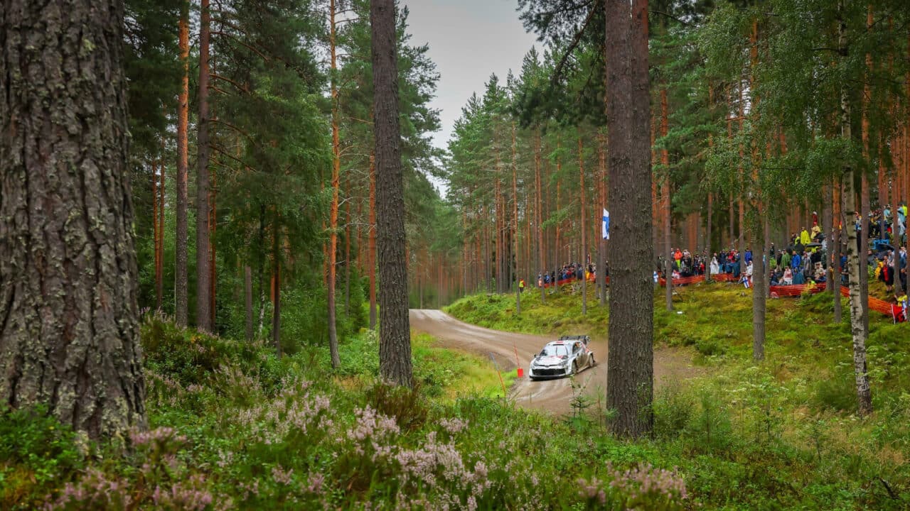 A rally car turns on a dirt road in a rainy forest.