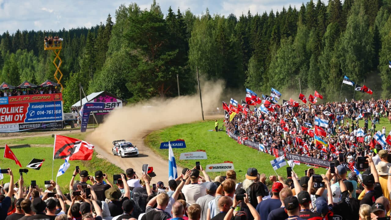 Rally car driving in front of the cheering audience.