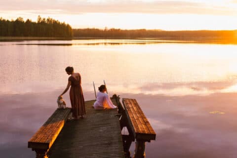 Kaksi henkilöä on laiturilla auringon laskiessa taustalla.