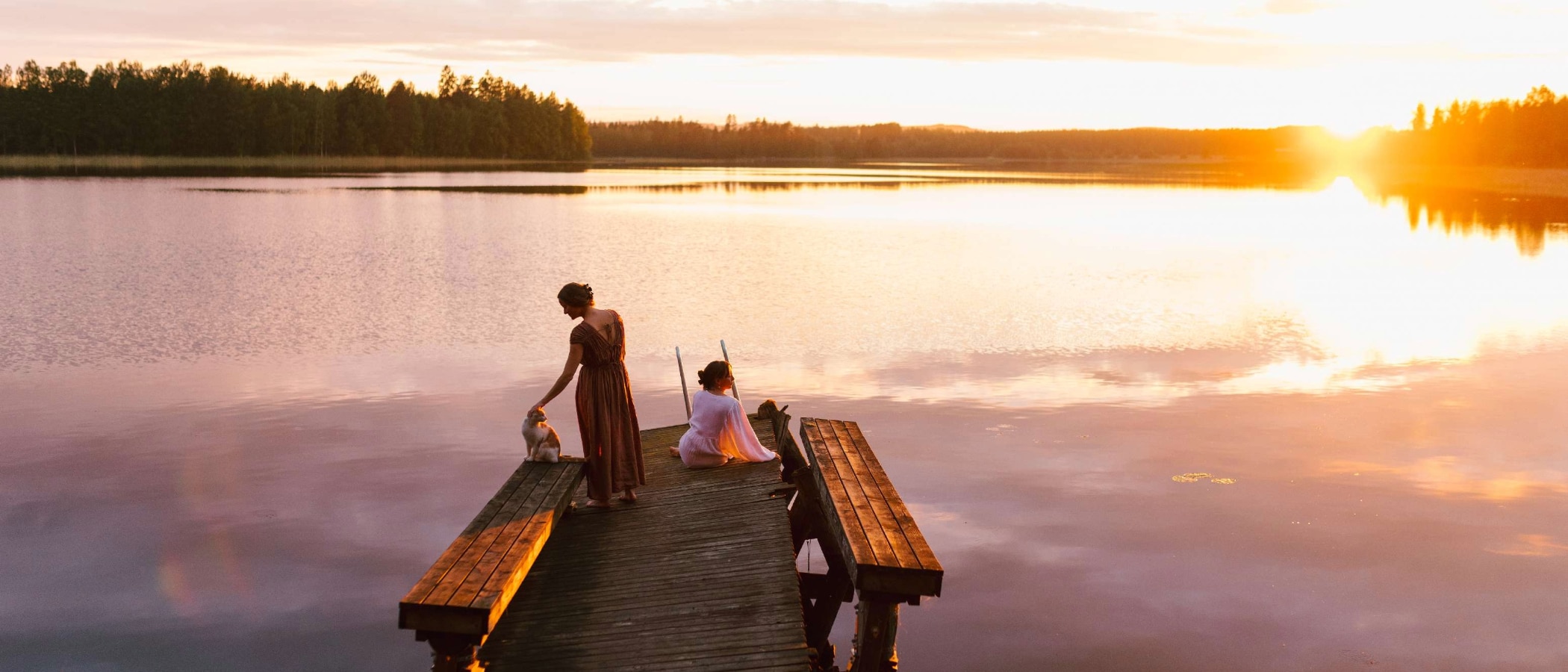 Kaksi henkilöä laiturinnokassa auringloaskun aikaan.
