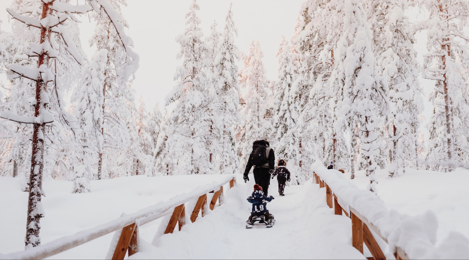 An adult and two children are walking through a snowy forest.