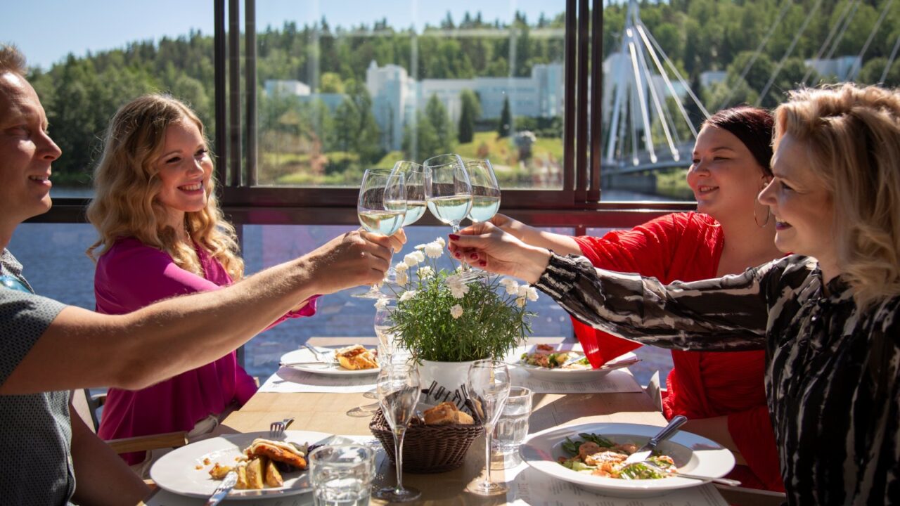 There are four people sitting around a restaurant table, all raising their glasses.