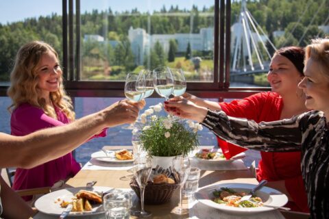 There are four people sitting around a restaurant table, all raising their glasses.