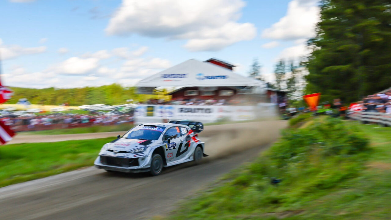 Ralliauto kiihdyttää hiekkatiellä.