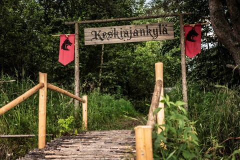 A wooden bridge and gate with a hanging sign saying Keskiajankylä