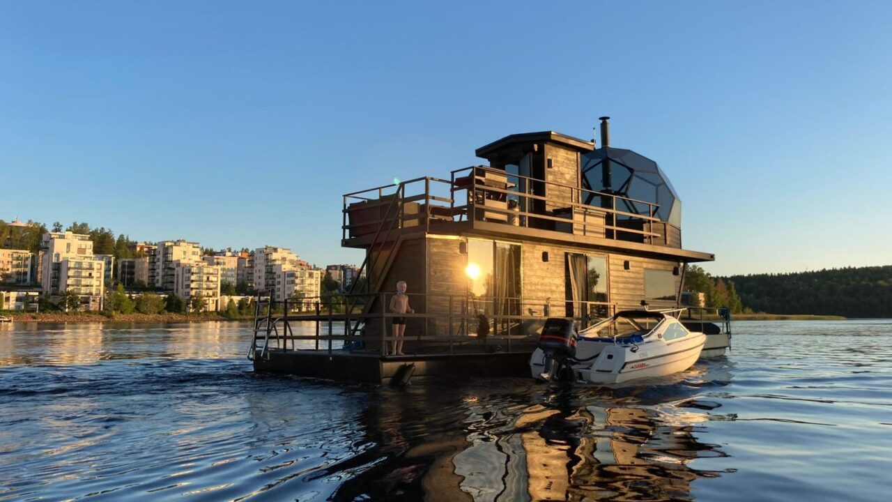 An igloo villa raft carrying a child and a motorboat in the middle of a lake in summer. Apartment buildings in the background.