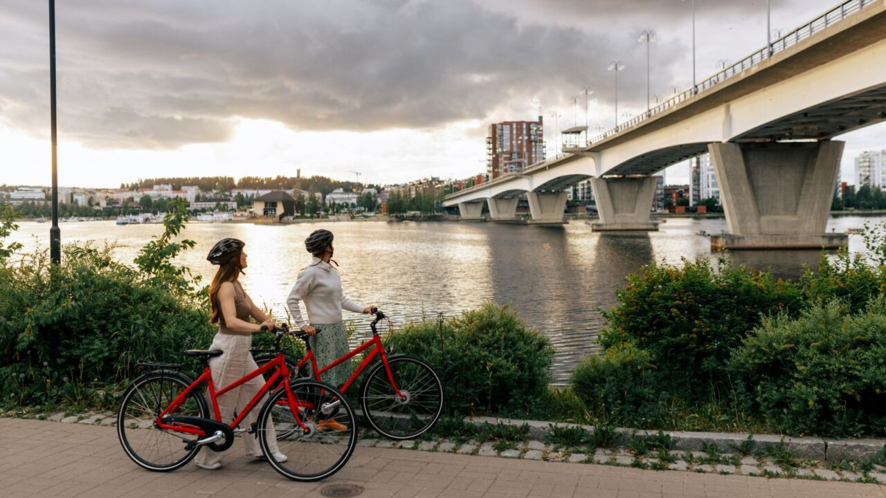 Kaksi henkilöä pyörien kanssa pysähdyksissä Rantaraitilla Kuokkalan sillan edustalla.