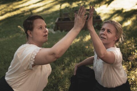 Two people are looking at their raised hands, the palms of which are almost touching