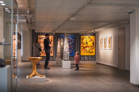 Visitors exploring an art exhibition at Keuruu Museum, featuring colorful paintings and sculptures.