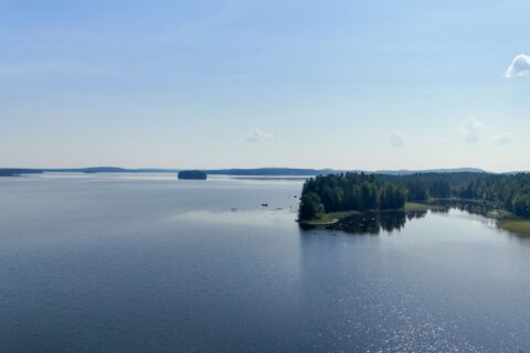 Kuvassa on järvi, jossa on muutamia saaria kesäpäivänä. Taivaalla on vain muutamia pilviä.