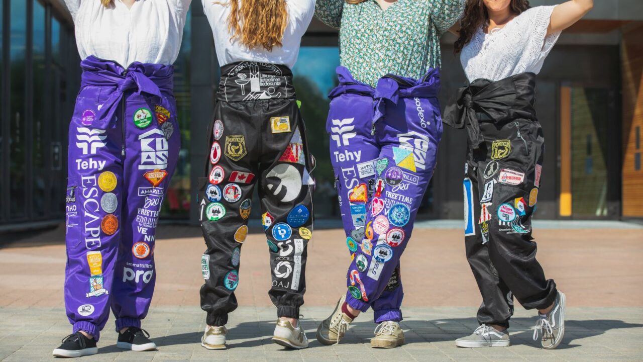 There are four persons in the photo, but the photo is cropped so that faces are not visible. The people are wearing colorful student overalls.