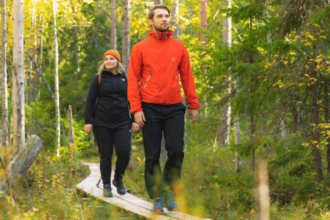 Kaksi henkilö kävelemässä pitkospuilla metsässä