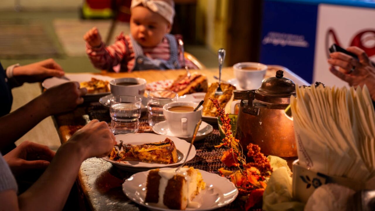 The photo shows refreshments on a coffee table and people eating